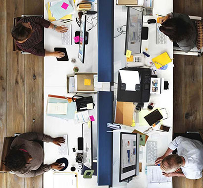 Overhead view of people sitting at an office workstation with computers and papers